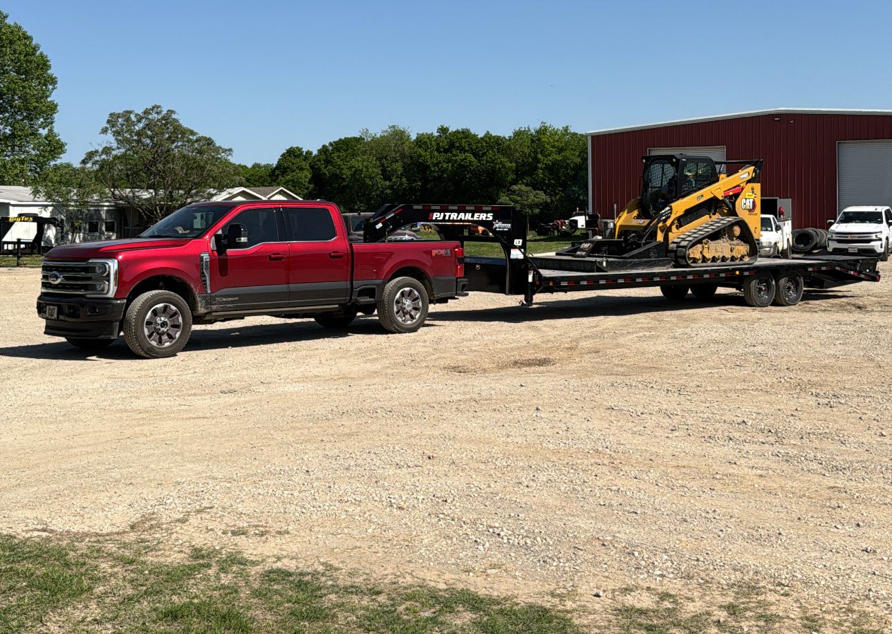 Red Ford F-250 hauling a CAT skid steer on a flatbed trailer