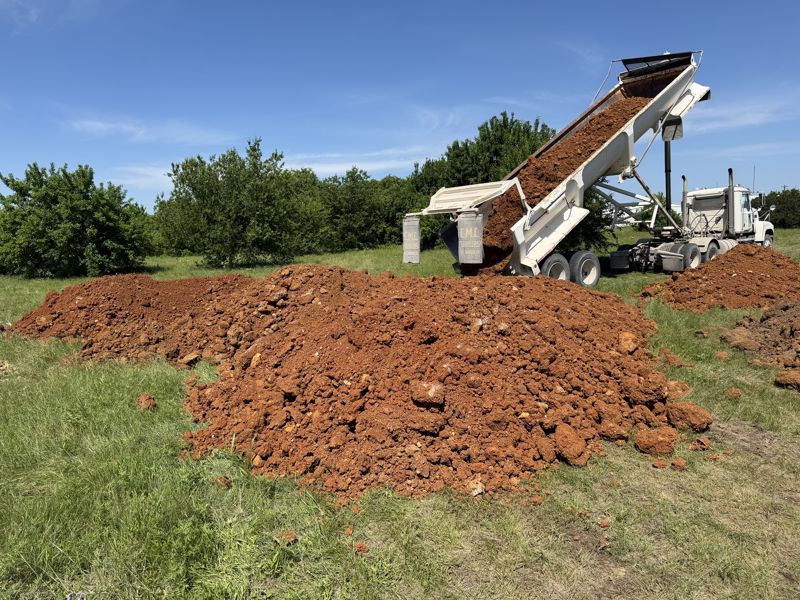 Red fill dirt dumped from a side dump in a field