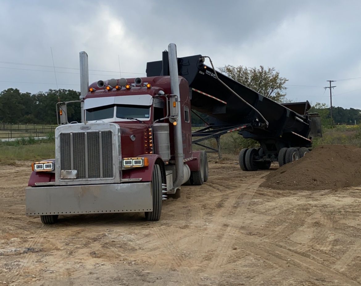 Maroon Peterbilt end dump unloading fill dirt