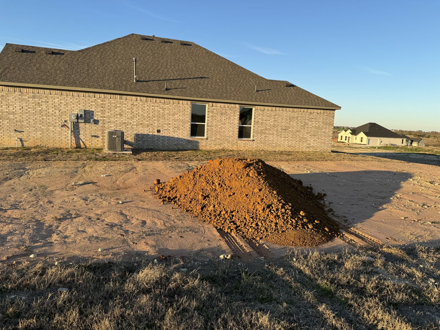 Red dirt pile beside a new brick home