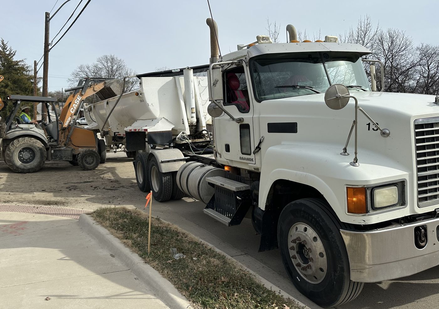 Backhoe loading a side dump on a city street